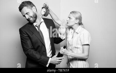 Nach Corporate Partei. Man Alkoholkrank. Böse Frau treffen betrunkenen Ehemann spät zu Hause. Geschäftsmann mit Alkohol Flasche und Frau mit Wecker. Süchtig Alkoholismus und Alkoholmissbrauch. Stockfoto