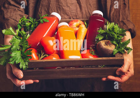 Frische Säfte Smoothies aus verschiedenen Gemüse Karotte apple Zuckerrüben, Tomaten in Flaschen in einer Holzkiste in weibliche Hände. Die Ernte. Kopieren Raum horizontal Stockfoto