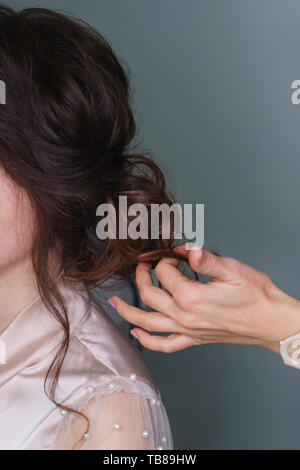 Friseur bei der Arbeit, die in den Prozess der Erstellung von Hochzeit Frisur. Hand Friseur begradigt braunen Locken. Perfekt und Schönheit im Detail. Schönheit Industrie Stockfoto