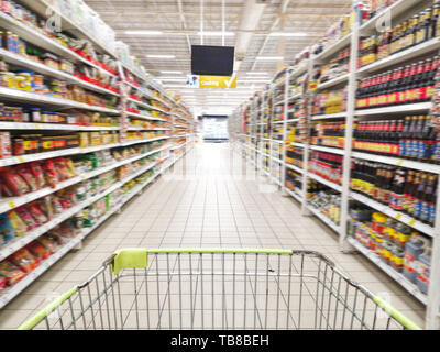 Warenkorb mit abstrakten verwischt Supermarkt Gang mit bunten Waren auf den Regalen im Hintergrund, Zeichen von Produkt für das Kochen hängen von der Decke Stockfoto