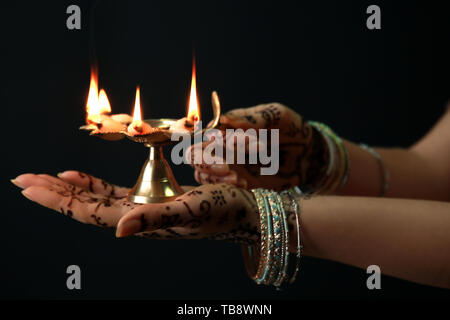 Weibliche Hände mit diya Lampe für die Feier des Divaly auf dunklem Hintergrund Stockfoto