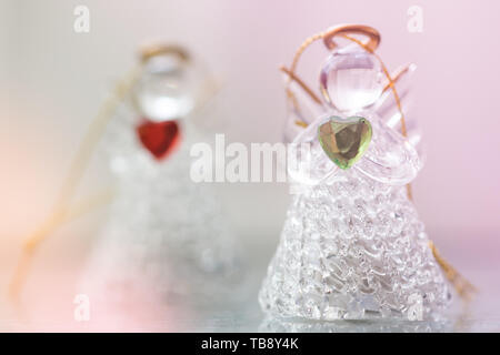 Zwei kleine Glasengel-Statuetten mit Herzen in den Händen. Das Konzept von Frieden und Liebe. Stockfoto