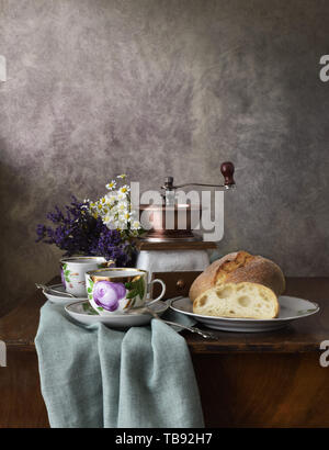 Retro still life Poster Frühstück. Vintage Kaffeemühle Tassen, silbernen Löffel, hausgemachtes Brot Bäckerei. Dark Light, Holztisch, Bettwäsche aus Geweben Stockfoto