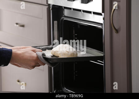 Frau putting Backblech mit rohen Teig für Brot in den Backofen Stockfoto