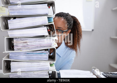Nahaufnahme einer Geschäftsfrau, die sich hinter den Stapel der Ordner auf dem Schreibtisch am Arbeitsplatz Stockfoto