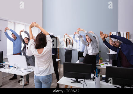 Glücklich, multi-ethnischen Geschäftsleute heben die Hände tun Stretching Übung im Büro Stockfoto