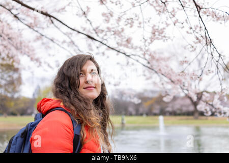 Tokio, Japan Yoyogi Park mit Jungen gerne touristische stehende Frau am Teich in der Innenstadt an bewölkten Tag unter dem Vordach von Sakura Blumen Stockfoto