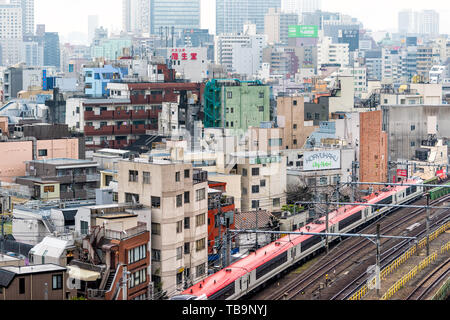 Tokyo, Japan - 30. März 2019: Shinjuku Stadtbild Blick Gebäude Wohngebiet an bewölkten grauen Nebel Nebel bewölkten Tag mit vielen Häusern und Roten Zug Stockfoto