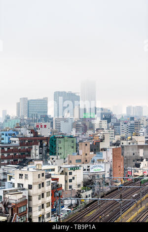 Tokyo, Japan - 30. März 2019: Shinjuku Stadtbild vertikale Ansicht Gebäude an bewölkten grauen Nebel Nebel bewölkten Tag mit vielen Häusern und Schienen Stockfoto