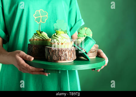 Junge Frau mit Board mit leckeren Kuchen und grünen Hut auf farbigen Hintergrund. St. Patrick's Day Celebration Stockfoto