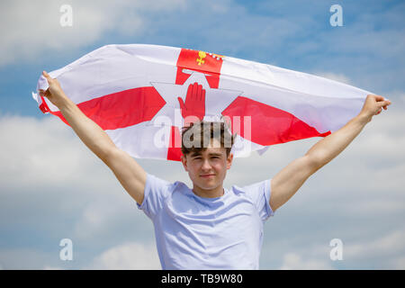 Junger Erwachsener, Kaukasier Männlich Holding am Strand halten Sie die Flagge Nordirland Stockfoto