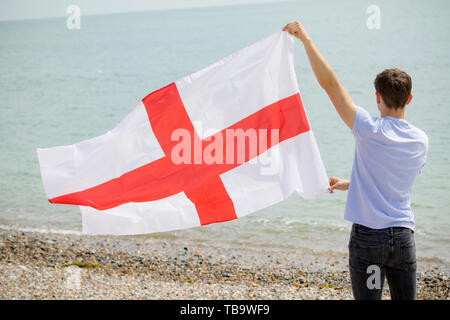 Junger Erwachsener, Kaukasier Männlich Holding am Strand halten die Flagge von England Stockfoto