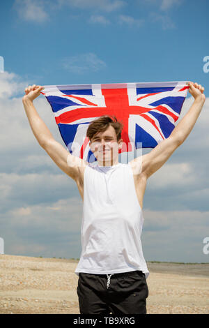 Junger Erwachsener, Kaukasier Männlich Holding an einem Strand Holding unter der Flagge von Großbritannien Stockfoto