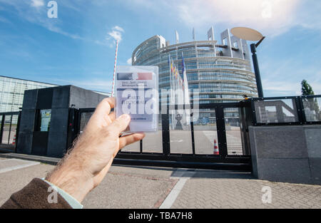 Straßburg, Frankreich, 26. Mai 2019: Mann hand Voter's Auto Französisch Carte Electorale am Eingang des Europäischen Parlaments zentrale Gebäude mit allen Flaggen auf den 2019 zu den Wahlen zum Europäischen Parlament Tag Stockfoto