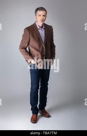 Bartgeier im mittleren Alter fashion model mit Business Casual Style Outfit für reife und zuversichtlich Schauen posieren. Die trendige Braune Jacke und Jeans und Armaturenbrett Stockfoto