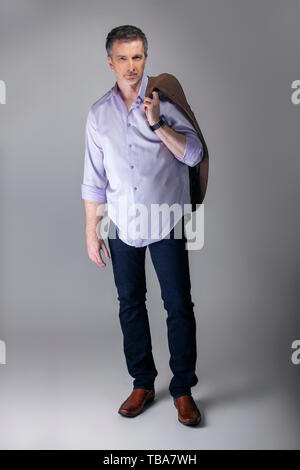 Im mittleren Alter Geschäftsmann tragen business casual Outfit. Der Mann posiert mit Untucked Langarm Shirt mit Jeans und eine Jacke. Zeigt m Stockfoto