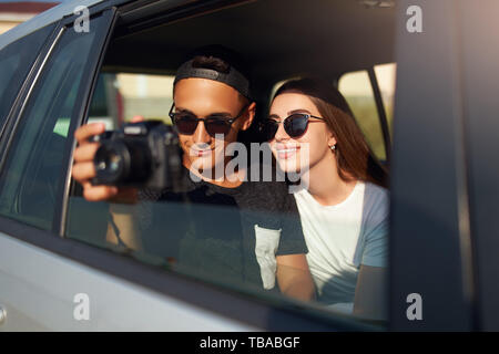 Blogger in Gläsern seiner Reise vlog Nehmen auf professionelle Kamera auf Road Trip. Mann Fotograf die Bilder aus offenen Fenster mit Freundin Stockfoto