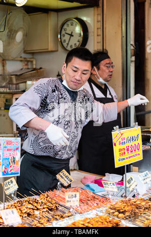 Tokyo, Japan - 30. März 2019: Äußere Markt in Tsukiji in der Nähe von Ginza mit glücklichen gegrillter Fisch Anbieter Mann auf der Straße und Melden Stockfoto