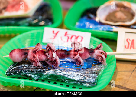 Tokio, Japan Straße in Tsukiji äußeren Markt in der Nähe von Ginza mit Nahaufnahme der Anzeige von Raw- oder gegrilltem Fisch, Tintenfisch essen Anbieter und Preis Stockfoto