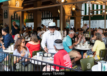 New Orleans, USA - 22. April 2018: Menschen im Café Du Monde Restaurant essen beignet Puderzucker Donuts und Zichorien Kaffee durch Kellner bedient Stockfoto