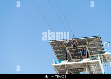 Destin, USA - 24. April 2018: Die niedrigen Winkel, Blick auf die zipline Turm mit Arbeiter und afrikanische amerikanische Frau fliegen und halten zu den Bars Griffe in Stockfoto