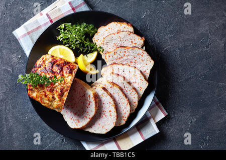 Huhn Terrine in Scheiben geschnitten serviert mit Zitronenscheiben und frischem Thymian auf einer schwarzen Platte auf einer konkreten Tabelle, Ansicht von oben, flatlay Stockfoto