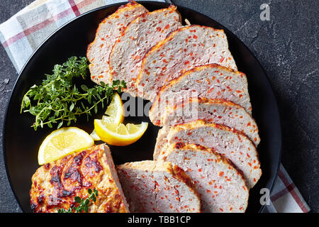 Close-up von geschnittenen Hähnchen Hackbraten serviert auf einem schwarze Platte mit Zitronenscheiben und frischem Thymian auf einer konkreten Tabelle, Ansicht von oben, flatlay, Makro Stockfoto