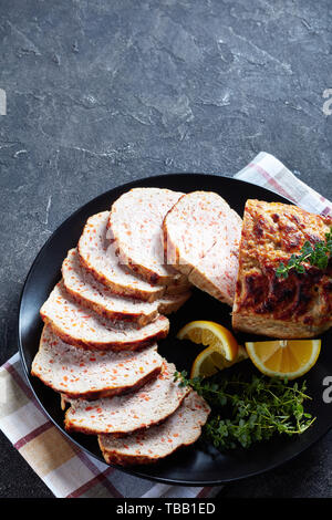 Close-up von geschnittenen Hähnchen Hackbraten auf eine schwarze Platte mit Zitronenscheiben und frischem Thymian auf einen konkreten Tisch serviert, vertikale Ansicht von oben Stockfoto