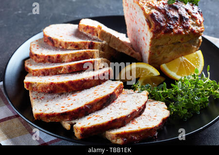 Close-up von geschnittenen Hähnchen Hackbraten serviert auf einem schwarze Platte mit Zitronenscheiben und frischem Thymian auf einer konkreten Tabelle, Ansicht von oben, Makro Stockfoto