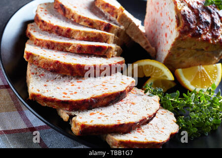 Close-up von geschnittenen Hähnchen Hackbraten auf eine schwarze Platte mit Zitronenscheiben und frischem Thymian auf einen konkreten Tisch serviert, horizontale Ansicht von oben Stockfoto