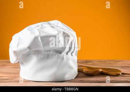 Kochmütze und Löffel auf hölzernen Tisch gegen Farbe Hintergrund Stockfoto