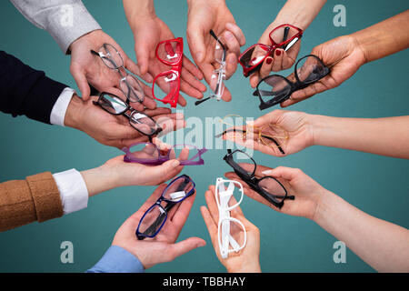 Blick von oben auf die Menschen an der Hand, die Vielzahl von Brillen gegen grüne Kulisse Stockfoto