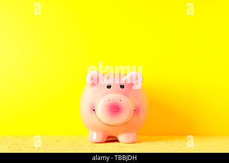 Happy Sparschwein auf gelb Tabelle gegen Farbe Hintergrund, Platz für Text. Finanzen, Geld sparen Stockfoto