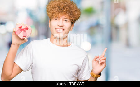 Jungen gutaussehenden Mann mit Herz Box als Geschenk zum Valentinstag sehr zufrieden zeigt mit Finger- und an der Seite Stockfoto