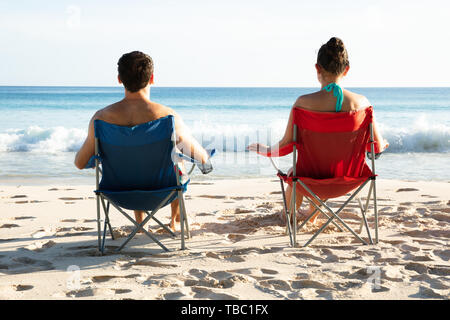 Ansicht der Rückseite des jungen Paares Sitzen auf Stühlen am blauen Meer am Strand. Stockfoto