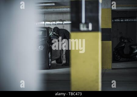 Auto Dieb in einer Aktion. Illegale Aktivitäten auf einem Parkplatz. Maskierte Männer zu stehlen, Moderne, kompakte Fahrzeug versuchen. Stockfoto