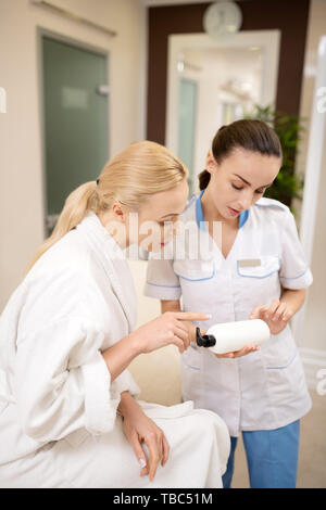 Beratung über Shampoo. Dunkelhaarige Schönheit Spezialist tragen einheitliche Beratung Kunden über Shampoo Stockfoto