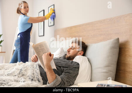 Faul mann lesen Zeitung, während seine Frau tut Chores zu Hause Stockfoto