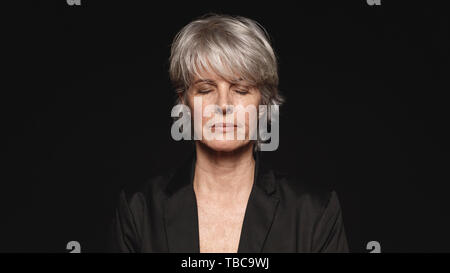Nahaufnahme der älteren Frau mit geschlossenen Augen. Frau in formale Abnutzung auf schwarzem Hintergrund isoliert. Stockfoto