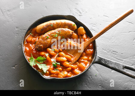 Nahaufnahme von gebackenen weiße Bohnen in Tomatensauce und gegrillte Würstchen in der Pfanne über schwarzen Tisch. Stockfoto