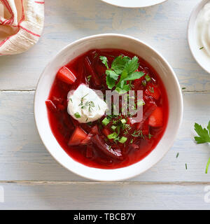 Russisch Ukrainisch-Suppe (Borschtsch) mit grünen und Sauerrahm. Rote-bete-Suppe in Schüssel auf weiße Holztisch. Ansicht von oben, flach Stockfoto