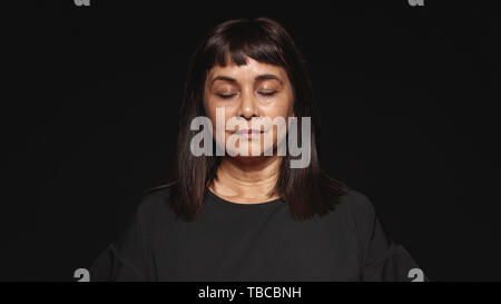 Nahaufnahme von Frau mittleren Alters mit geschlossenen Augen. Woman in Black Dress auf schwarzem Hintergrund isoliert. Stockfoto