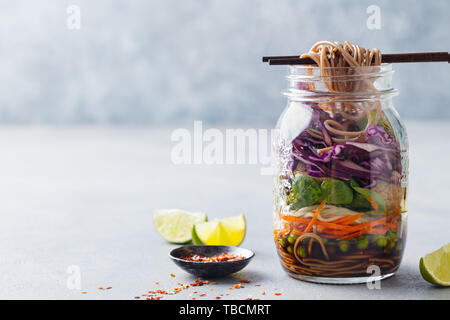 Gesunde Asiatischer Salat mit Nudeln, Gemüse, Huhn und Tofu im Glas. Grauer Hintergrund. Kopieren Sie Platz. Stockfoto