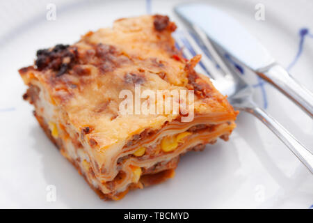 Stück Lasagne auf einem Teller mit Messer und Gabel. Schließen Sie herauf Bild. Stockfoto