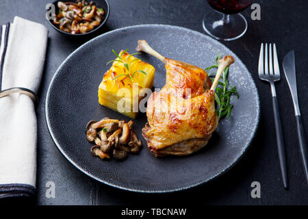 Entenschenkel Confit mit Kartoffelgratin und Pilz auf einem Teller. Schiefer Hintergrund. Stockfoto