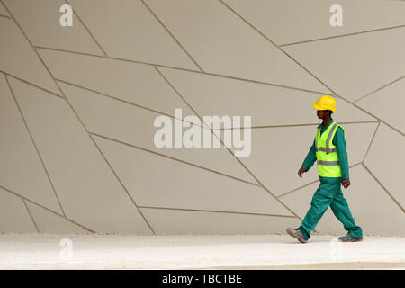 Doha, Katar - 11 April, 2019: Ein Arbeiter mit einer Berufsbekleidung und eine einheitliche Spaziergänge rund um die National Museum von Qatar. Stockfoto