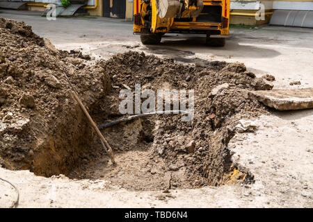 Grube von einem Bagger ausgegraben. Reparaturarbeiten im Innenhof eines Wohnhauses. Stockfoto