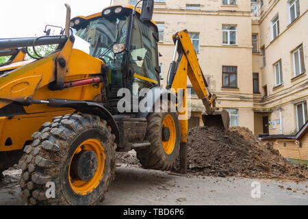 Bagger gräbt ein Graben. Reparaturarbeiten im Innenhof eines Wohnhauses. Stockfoto
