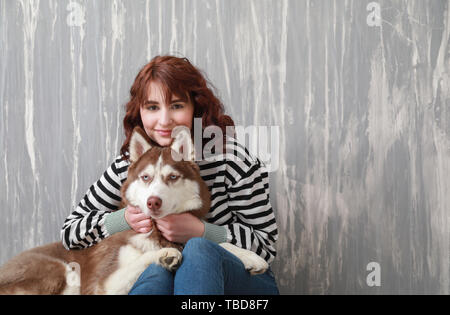 Junge Frau mit ihrem niedlichen Hund in der Nähe der graue Wand Stockfoto