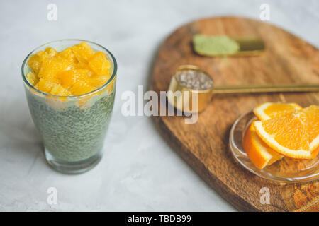 Matcha Grüntee Chia Samen pudding Dessert mit Orange in ein Glas. Nahaufnahme, Ansicht von oben, flach. Superfood und veganes Essen Konzept. Grauer Hintergrund, Co Stockfoto